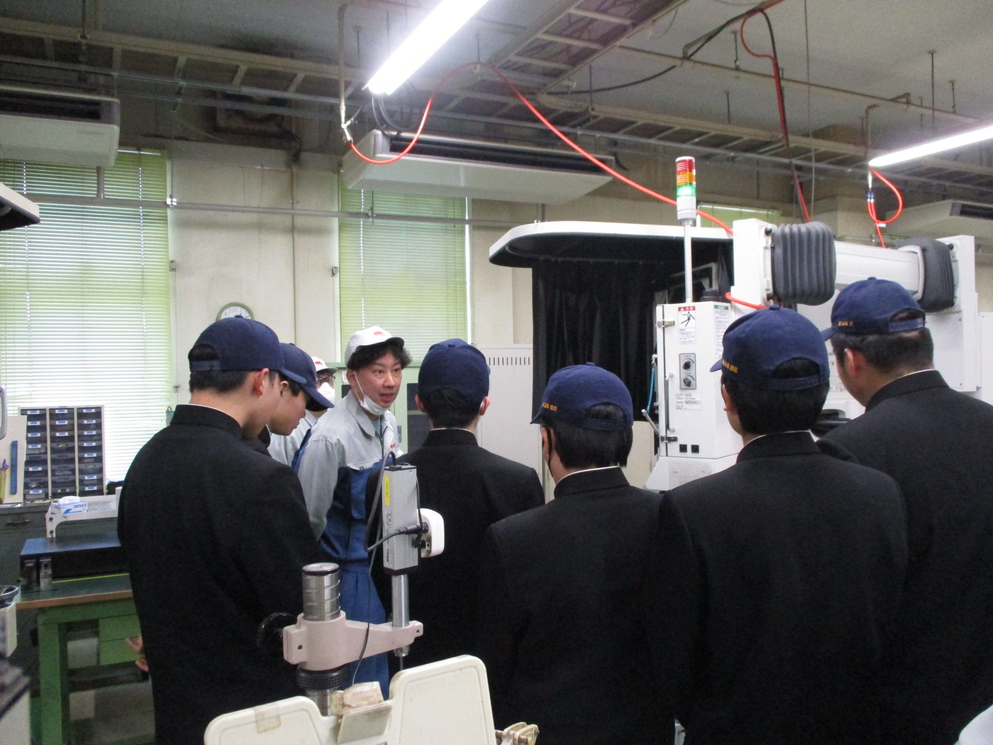 研削加工機の説明を受ける高校生の後ろ姿