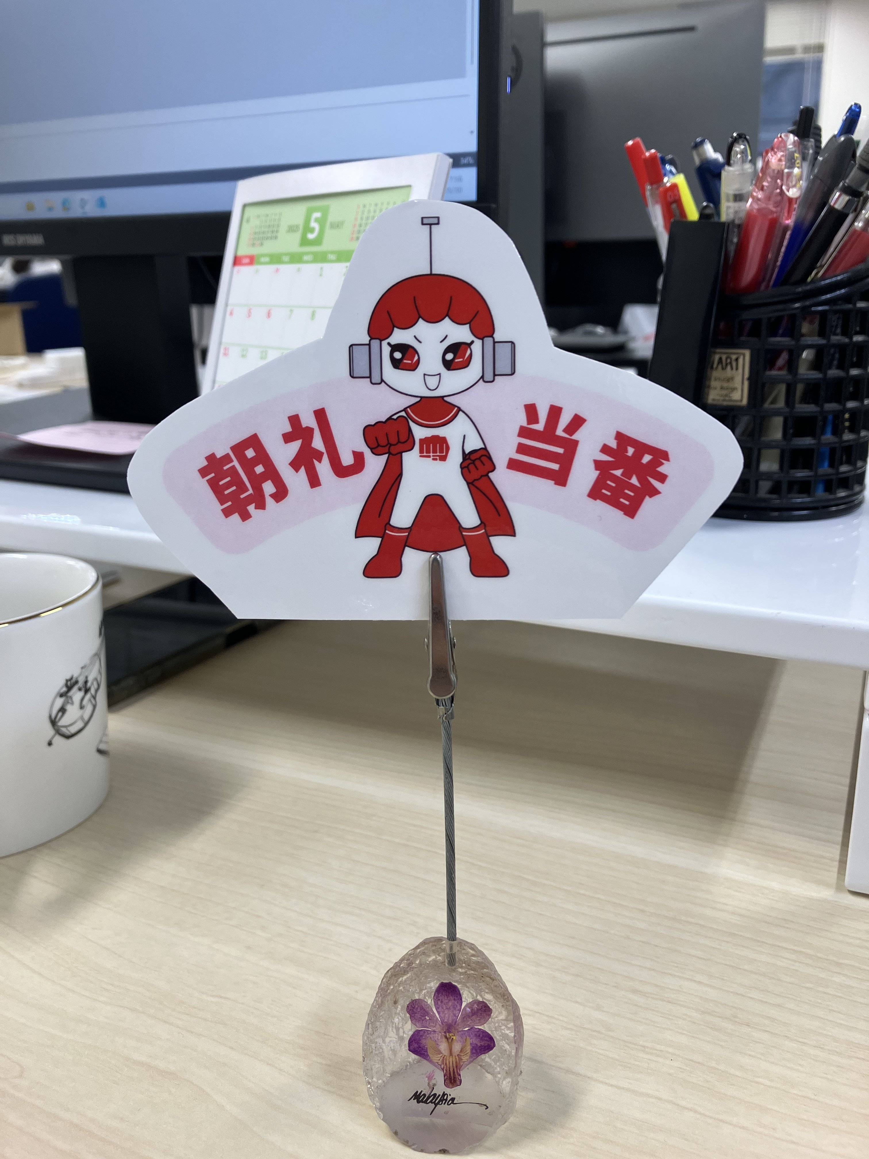 デスク上にパンチマンのイラストと「朝礼当番」と文字が書かれた札が立てられている